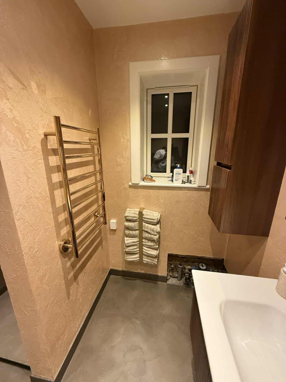 Badeværelse med varm sandfarvet microcement på vægge og gråt microcement-gulv med guldhåndklædetørrer